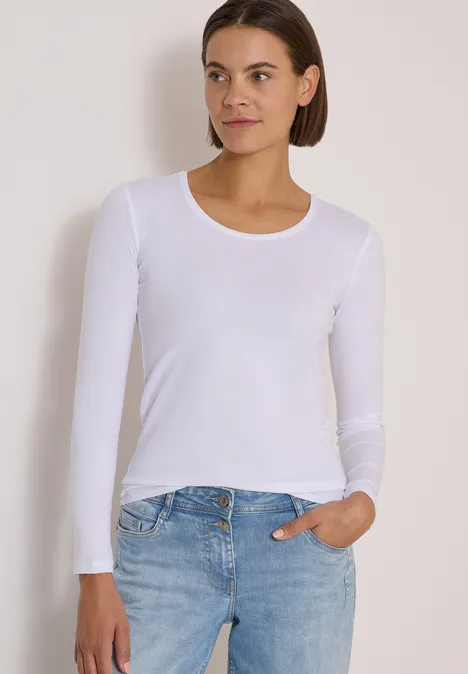 Basic Shirt mit Rundhals im 2er-Pack urban dark blue/white Eine Frau in weißem Langarmshirt und blauen Jeans steht vor neutralem Hintergrund.