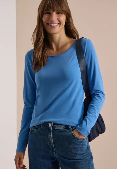 Frau lächelnd in blauem Langarmshirt und Jeans mit Umhängetasche