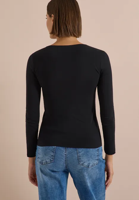 Frau in schwarzem Langarmshirt und blauer Jeans von hinten fotografiert.