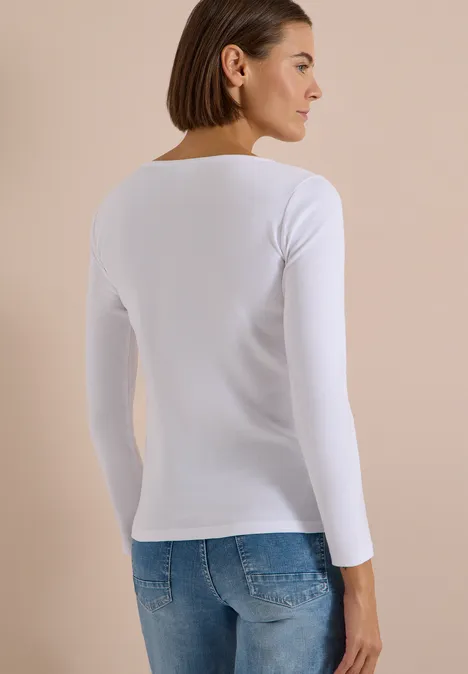 Frau von hinten mit weißem Langarmshirt und blauen Jeans vor dezentem Hintergrund.