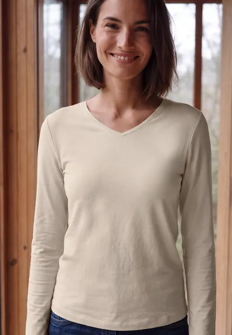 Longsleeve met V-hals cashmere beige Eine lächelnde Frau vor einem Fenster, trägt cremefarbenes, langärmliges V-Neck-Shirt.