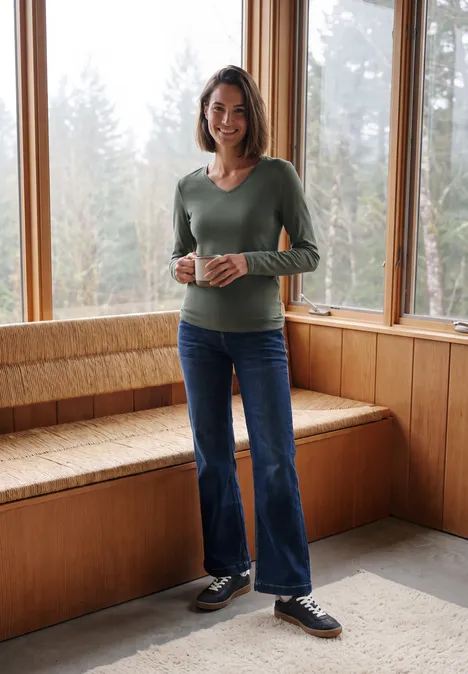 Langarm Shirt in Unifarbe mit V-Neck dried olive green Frau steht in holzvertäfeltem Raum an großen Fenstern und hält eine Tasse.