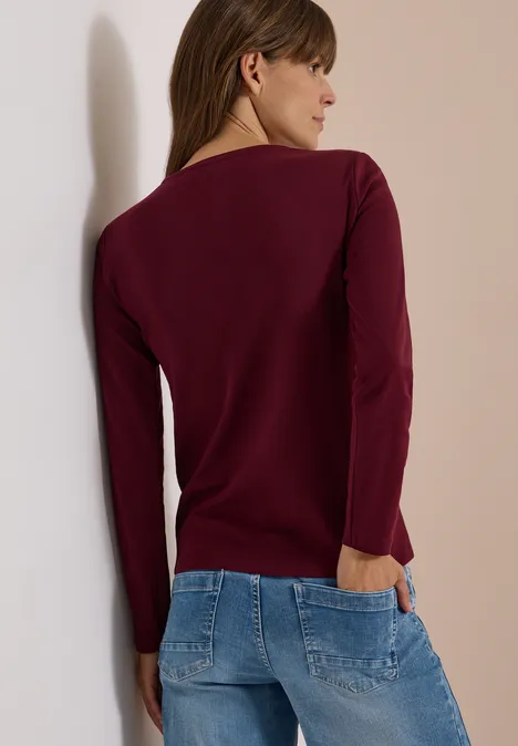 Langarm Shirt in Unifarbe mit V-Neck red wine Frau von hinten in bordeauxrotem Pullover und hellblauen Jeans, mit einer Hand in der Gesäßtasche.