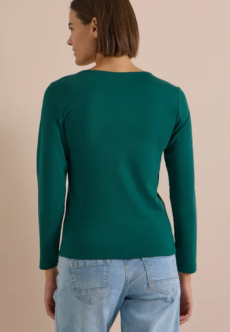 Rückenansicht einer Frau in grünem Langarmshirt und blauen Jeans.