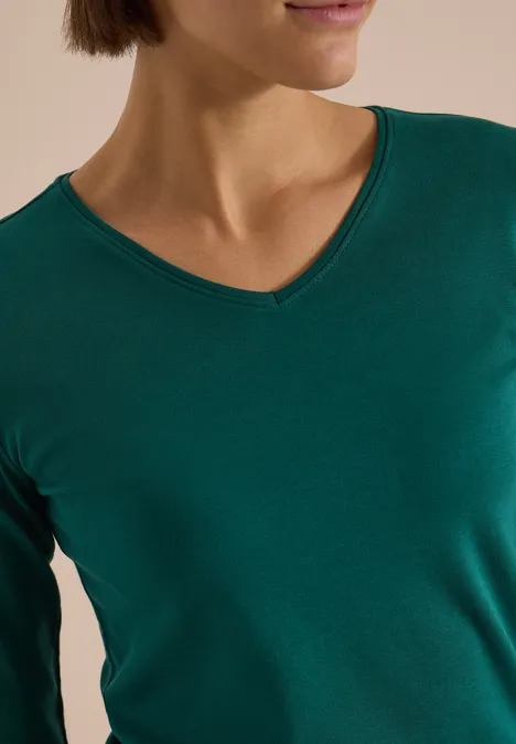 Frau mit grünem V-Ausschnitt-Shirt, nur Schultern und unterer Teil des Gesichts sichtbar.