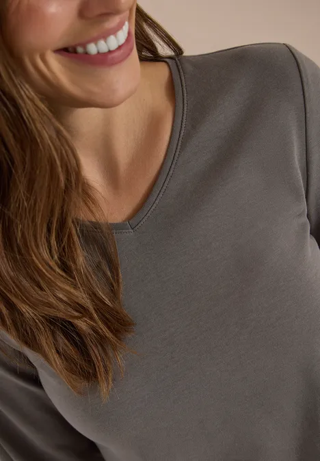 Nahaufnahme einer lächelnden Frau in einem grauen Langarmshirt.