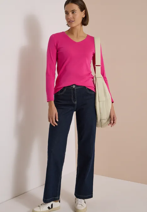 Langarm Shirt in Unifarbe mit V-Neck pink flash Frau mit pinkem Pullover, weiten Jeans und beiger Tasche vor hellem Hintergrund.