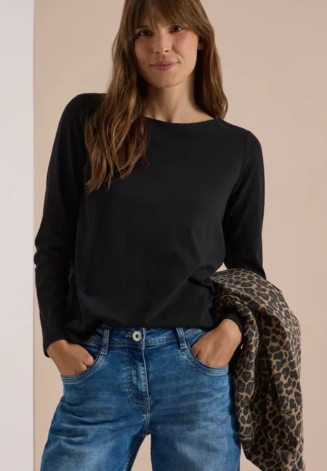 Langarm Shirt mit U-Boot-Ausschnitt Black Eine Frau in schwarzem Langarmshirt und blauer Jeans hält lässig eine gemusterte Jacke über dem Arm.