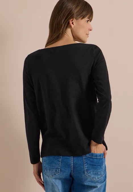 Langarm Shirt mit U-Boot-Ausschnitt Black Eine Frau in schwarzem Langarmshirt und blauen Jeans, von hinten, mit einer Hand in der Tasche.
