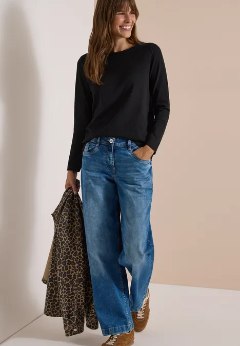 Langarm Shirt mit U-Boot-Ausschnitt Black Frau trägt schwarzen Langarmshirt, weite Jeans und braune Stiefeletten, hält Leopardenjacke.