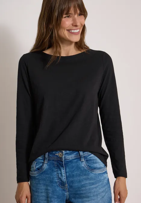 Langarm Shirt mit U-Boot-Ausschnitt Black Frau in schwarzem Langarmshirt und blauen Jeans, lächelnd vor neutralem Hintergrund.
