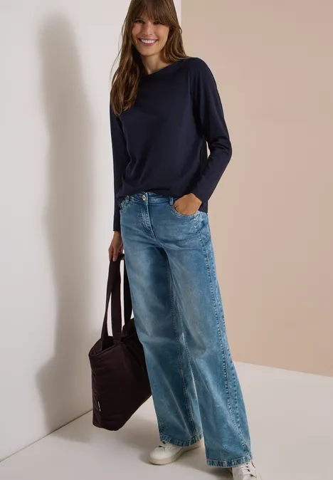 Langarm Shirt mit U-Boot-Ausschnitt urban dark blue Frau mit dunkelblauem Pullover, weitem Jeans und weißen Sneakern, lächelnd, trägt eine braune Tasche.