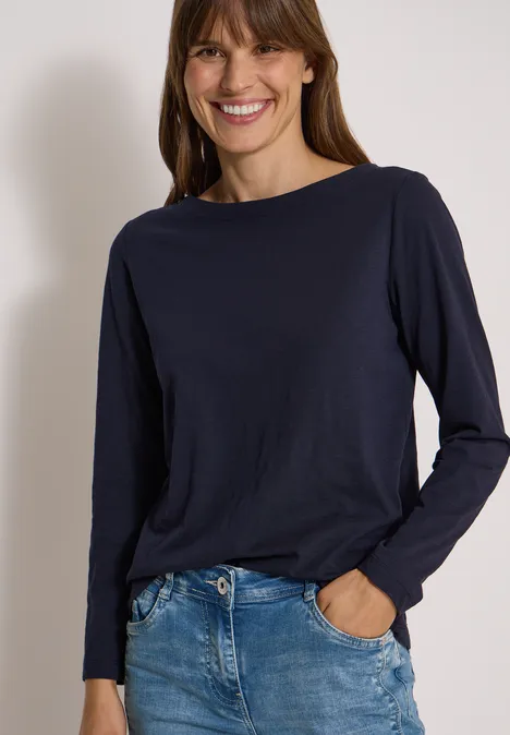 Langarm Shirt mit U-Boot-Ausschnitt urban dark blue Frau im dunkelblauen Langarmshirt und Jeans, die lächelnd vor weißem Hintergrund posiert.