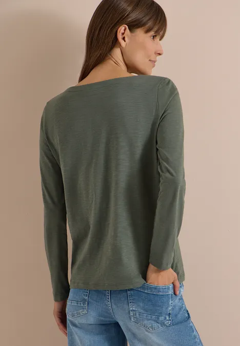 Langarm Shirt mit U-Boot-Ausschnitt dried olive green Frau mit langen braunen Haaren in olivgrünem Langarmshirt, Rückenansicht, Hände in Jeans-Taschen.