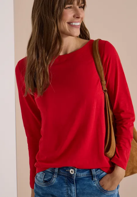 Langarm Shirt mit U-Boot-Ausschnitt flame red Lächelnde Frau im roten Langarmshirt trägt lockere Hose und Schultertasche vor neutralem Hintergrund.