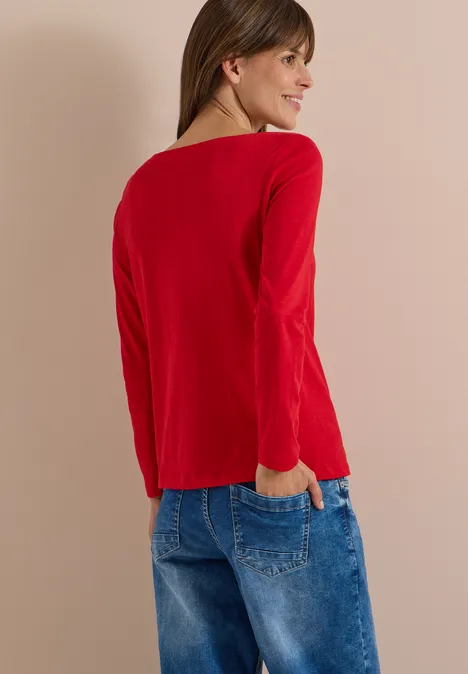 Langarm Shirt mit U-Boot-Ausschnitt flame red Eine Frau steht von hinten in einem roten Langarmshirt und blauen Jeans vor hellem Hintergrund.
