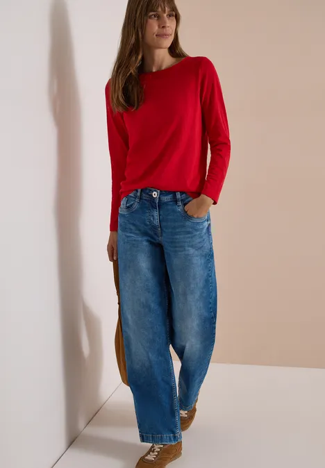 Langarm Shirt mit U-Boot-Ausschnitt flame red Frau in rotem Pullover und weiter Jeanshose vor neutralem Hintergrund.