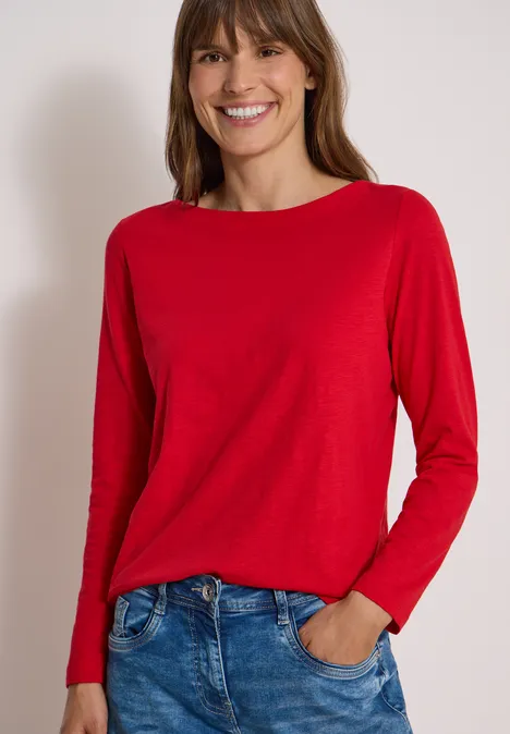 Langarm Shirt mit U-Boot-Ausschnitt flame red Frau mit langen braunen Haaren in rotem Langarmshirt und Jeans, lächelnd vor neutralem Hintergrund