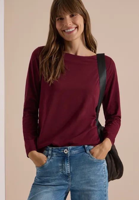 Langarm Shirt mit U-Boot-Ausschnitt red wine Junge Frau in Jeans und bordeauxrotem Langarmshirt, lächelt, Hände in Hosentaschen, trägt Schultertasche.