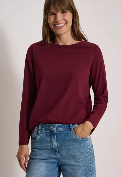 Langarm Shirt mit U-Boot-Ausschnitt red wine Eine lächelnde Frau trägt ein bordeauxfarbenes Langarmshirt und Jeans.