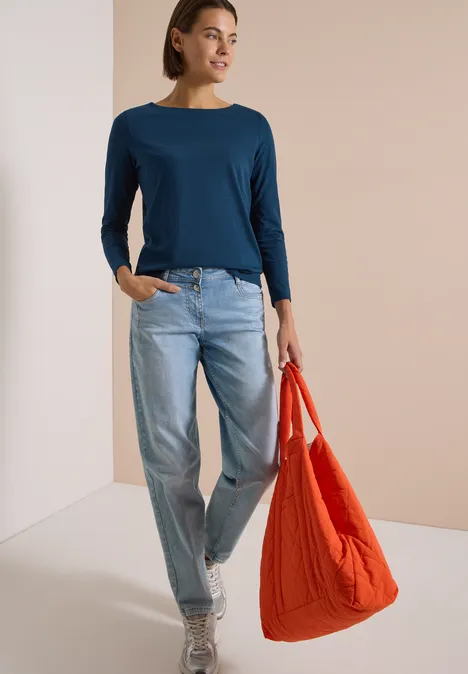 Langarm Shirt mit U-Boot-Ausschnitt moonlight blue Frau in blauem Langarmshirt, hellen Jeans und weißen Schuhen trägt eine große rote Tasche vor neutralem Hintergrund.