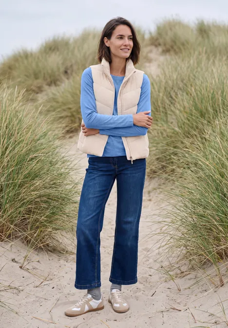 T-shirt à manches longues et col bateau north blue Frau in Jeans, blauem Shirt und beige Weste steht lächelnd in Sanddünen.