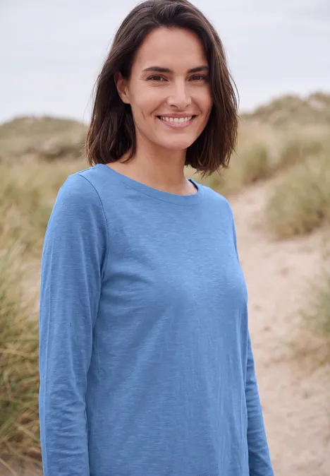 T-shirt à manches longues et col bateau north blue Lächelnde Frau in blauem Shirt steht am Dünenstrand und schaut in die Kamera.