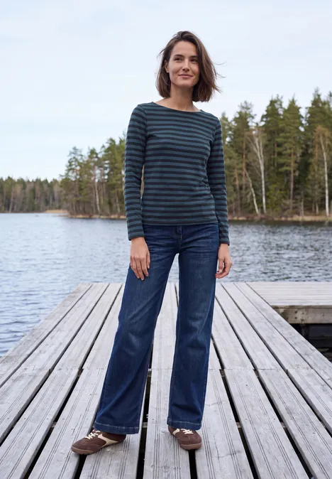 Langarm Shirt mit Boat Neck und Streifen urban dark blue Frau steht auf Holzsteg am See, trägt gestreiftes Shirt und Jeans.