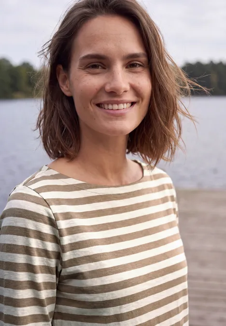 Lachende vrouw in gestreept shirt voor een rustig meer in de buitenlucht.
