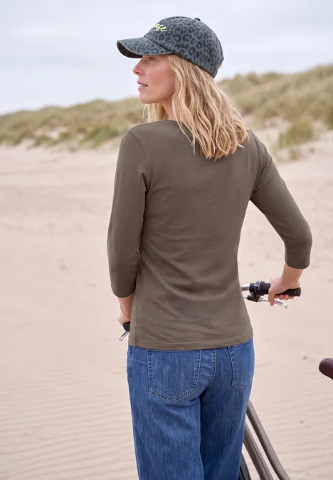 Femme coiffée d'une casquette pousse son vélo le long des dunes de sable sur la plage.
