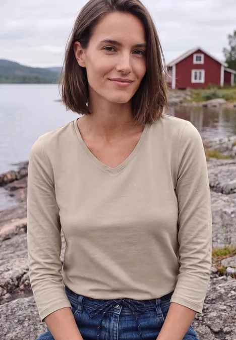 Jeune femme au bord d’un lac, derrière elle une maison rouge et une eau paisible.