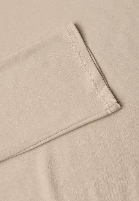Tissu beige ou t-shirt plié avec couture visible, posé sur une surface lisse