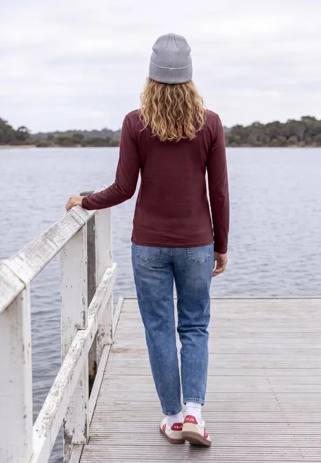 Une personne en bonnet se tient sur une jetée et regarde le lac.