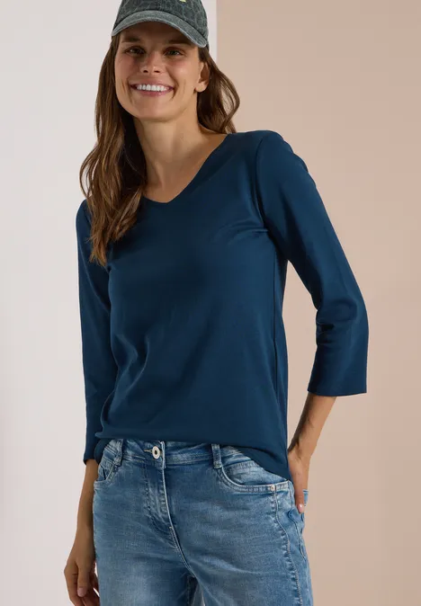 3/4-Arm Shirt in Unifarbe mit V-Neck moonlight blue Frau in blaugrünem 3/4-Arm-Shirt, Jeans und Cap lächelt.