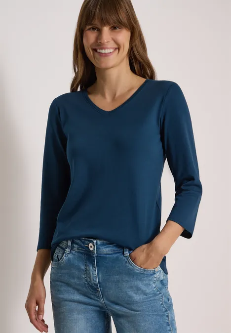 3/4-Arm Shirt in Unifarbe mit V-Neck moonlight blue Eine lächelnde Frau mit halblangem Haar trägt ein dunkelblaues V-Shirt und Jeans vor weißem Hintergrund.