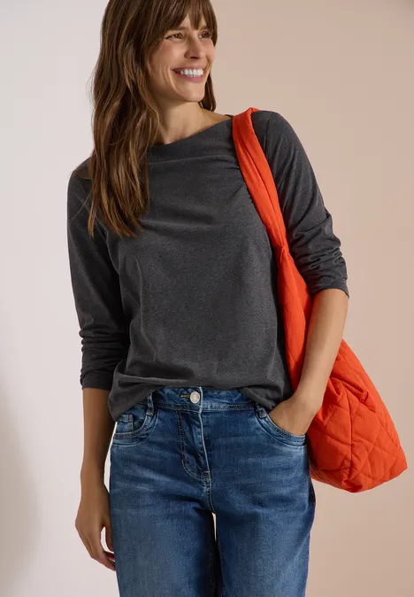 Langarm Shirt mit U-Boot-Ausschnitt black melange Eine Frau in grauem Langarmshirt und Jeans trägt lächelnd eine orangefarbene Tasche über der Schulter.
