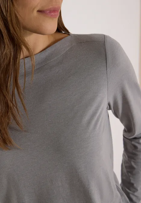 Vorderansicht einer Frau in grauem Langarmshirt, Oberkörper und Teil des Gesichts sichtbar.