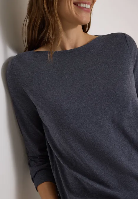 Langarm Shirt mit U-Boot-Ausschnitt urban dark blue melange Frau lehnt an weiße Wand, trägt dunkelgraues Langarmshirt und lächelt leicht.