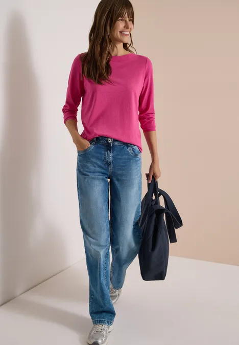 Langarm Shirt mit U-Boot-Ausschnitt pink flash melange Frau mit pinkem Pullover, weiter Jeans und dunkler Tasche steht lächelnd in Zimmerecke.