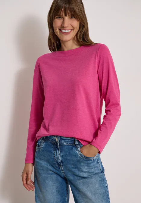 Langarm Shirt mit U-Boot-Ausschnitt pink flash melange Eine lächelnde Frau in pinkem Langarmshirt und Jeans steht entspannt, eine Hand in der Hosentasche.