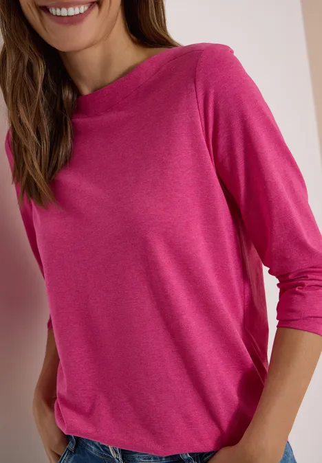 Langarm Shirt mit U-Boot-Ausschnitt pink flash melange Frau in locker sitzendem pinken 3/4-Arm-Shirt, lächelnd mit Händen in den Taschen.