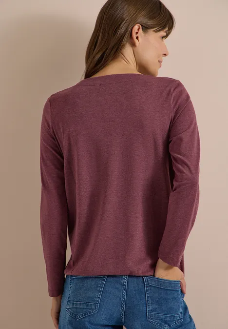 Langarm Shirt mit U-Boot-Ausschnitt red wine melange Eine Frau steht seitlich abgewandt im purpurnen Langarmshirt und blauer Jeans vor beigem Hintergrund.