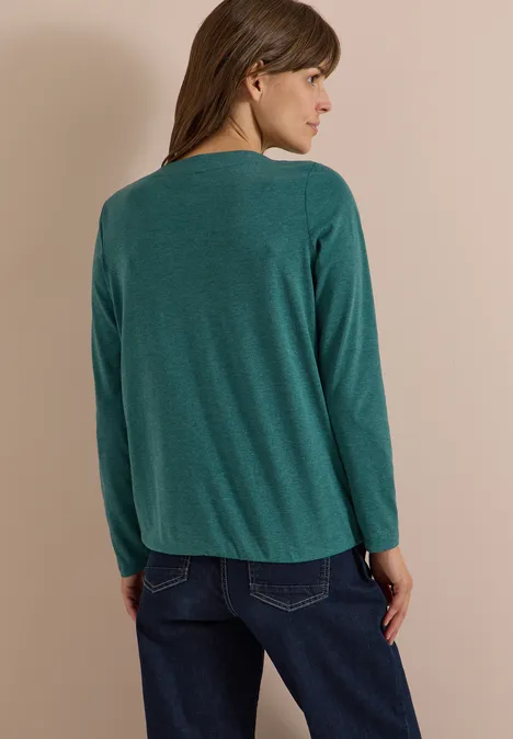 Langarm Shirt mit U-Boot-Ausschnitt dark fir green melange Frau von hinten in grüner Langarmbluse und blauen Jeans vor neutralem Hintergrund.
