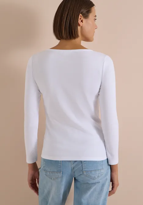 Langarm Shirt mit U-Boot-Ausschnitt White Frau von hinten in weißem Langarmshirt und Jeans vor beigem Hintergrund.
