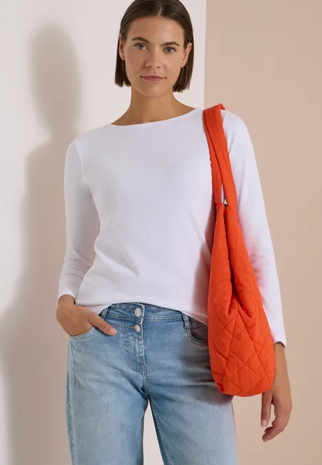 Langarm Shirt mit U-Boot-Ausschnitt White Frau in weißem Longsleeve und Jeans mit orangefarbener Stepp-Tasche vor hellem, neutralem Hintergrund.