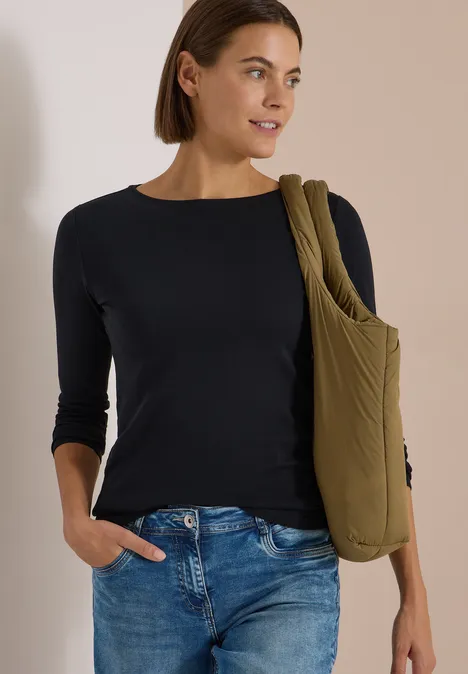 Langarm Shirt mit U-Boot-Ausschnitt Black Frau trägt schwarzen Dreiviertelarm-Pullover, Jeans und eine olivgrüne Umhängetasche.