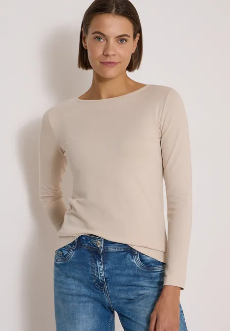 Langarm Shirt mit U-Boot-Ausschnitt cashmere beige Eine Frau trägt ein beigefarbenes Langarmshirt und blaue Jeans vor weißem Hintergrund.