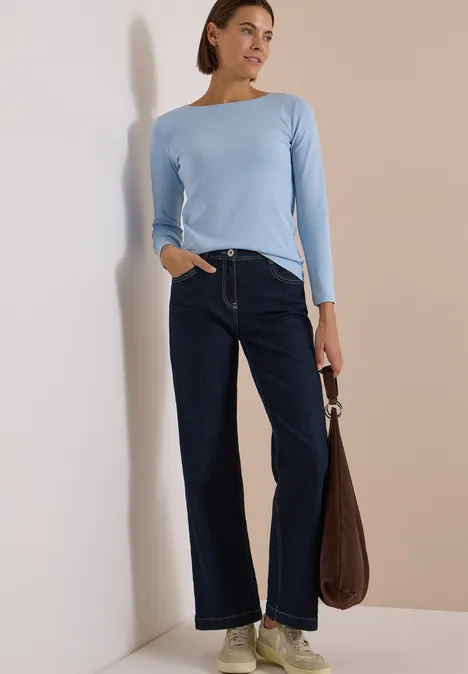 Langarm Shirt mit U-Boot-Ausschnitt cosmopolitan blue Frau steht mit hellblauem Langarmshirt, weiten dunklen Jeans und brauner Tasche vor einer Wand.
