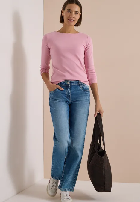 Langarm Shirt mit U-Boot-Ausschnitt mellow rose Eine Frau in rosa Longsleeve, blauen Jeans und weißen Sneakers trägt vor schlichter Wand eine schwarze Tasche.