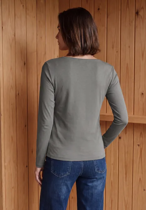 Frau von hinten in grauem Langarmshirt und Jeans vor Holzwand.